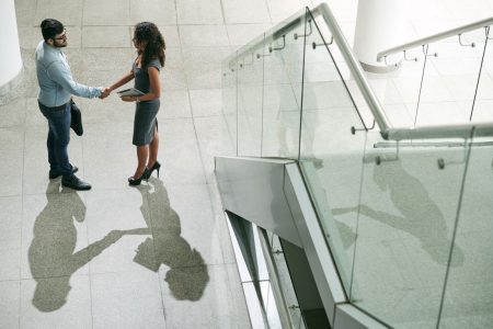 businesswoman and businessman shaking hands at bottom of office stairs
