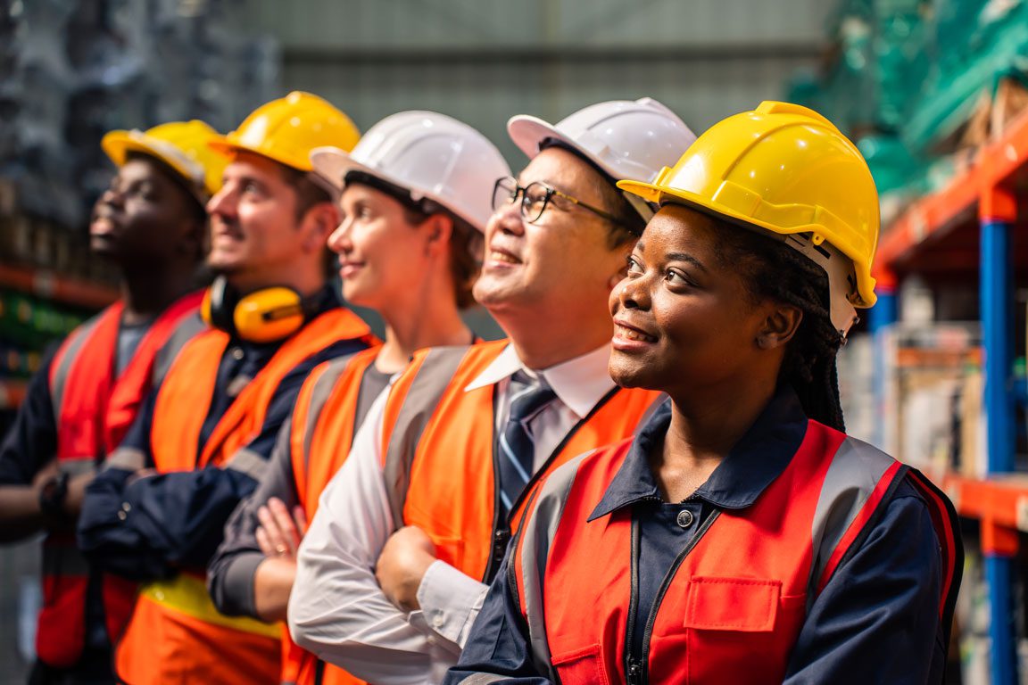 a diverse group of men and women looking up to the left, smiling and wearing construction outfits